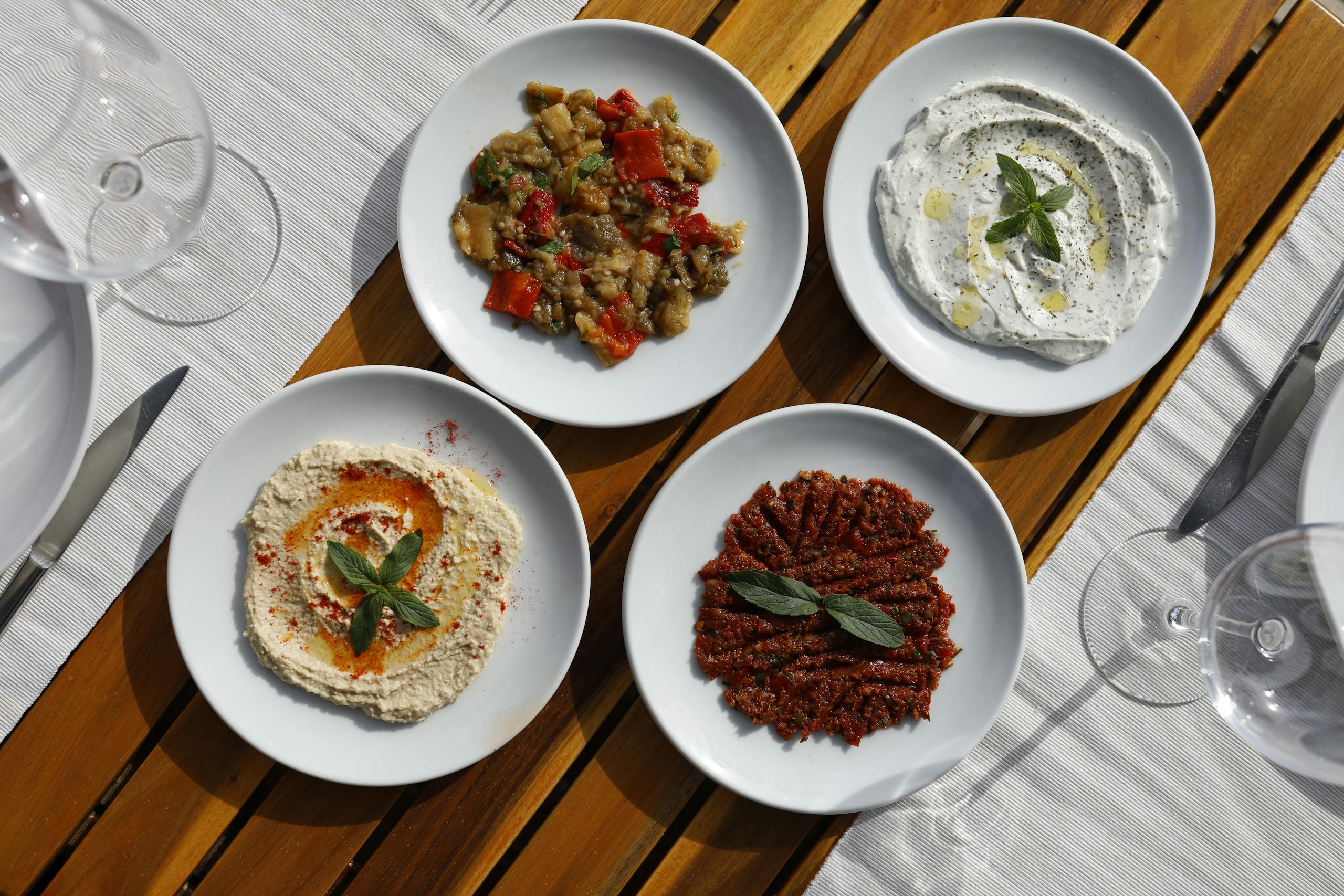 Aerial view of Mediterranean meze with diverse dips on white plates, outdoors.
